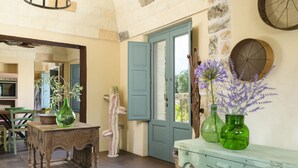 Een rustiek interieur met een houten tafel, een groene vaas met bloemen, een blauwe deur en een stenen muur.