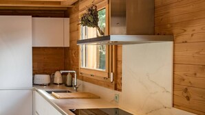 A modern kitchen with wooden beams, white cabinetry, a stainless steel range hood, and a window with a view of greenery. - Semi-detached chalet near the slopes with sauna (LA TOUSSUIRE)