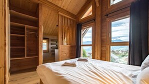 A wooden cabin bedroom with a bed, a built-in wardrobe, and large windows offering a view of the mountains. - Semi-detached chalet near the slopes with sauna (LA TOUSSUIRE)