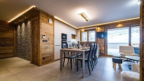 A modern kitchen with wooden accents, a dining area with chairs and a table, and a view of the outside.