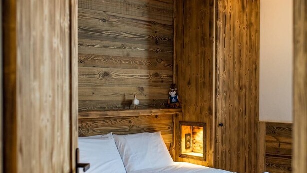 A wooden room with a bed, a nightstand, and a wall-mounted light fixture.