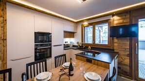 A modern kitchen with a built-in oven, a dining table set for four, and a large window overlooking a deck.