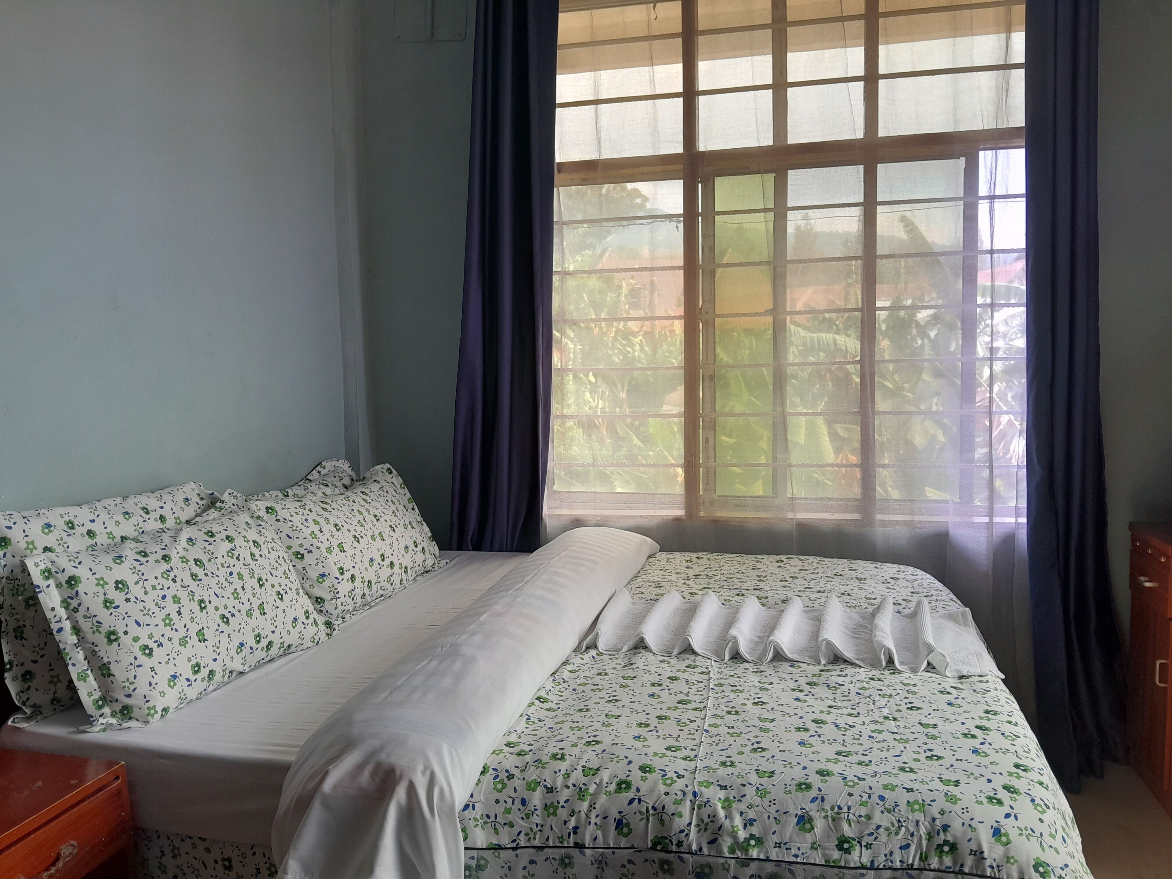 A room with a bed, a wooden nightstand, and a window with curtains.
