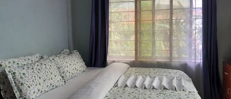 A room with a bed, a wooden nightstand, and a window with curtains.