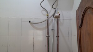 A bathroom with a white tiled wall, a wooden door, and a wall-mounted water heater. - HIGHLAND BREEZE AVACADO HOTEL (Mbeya)
