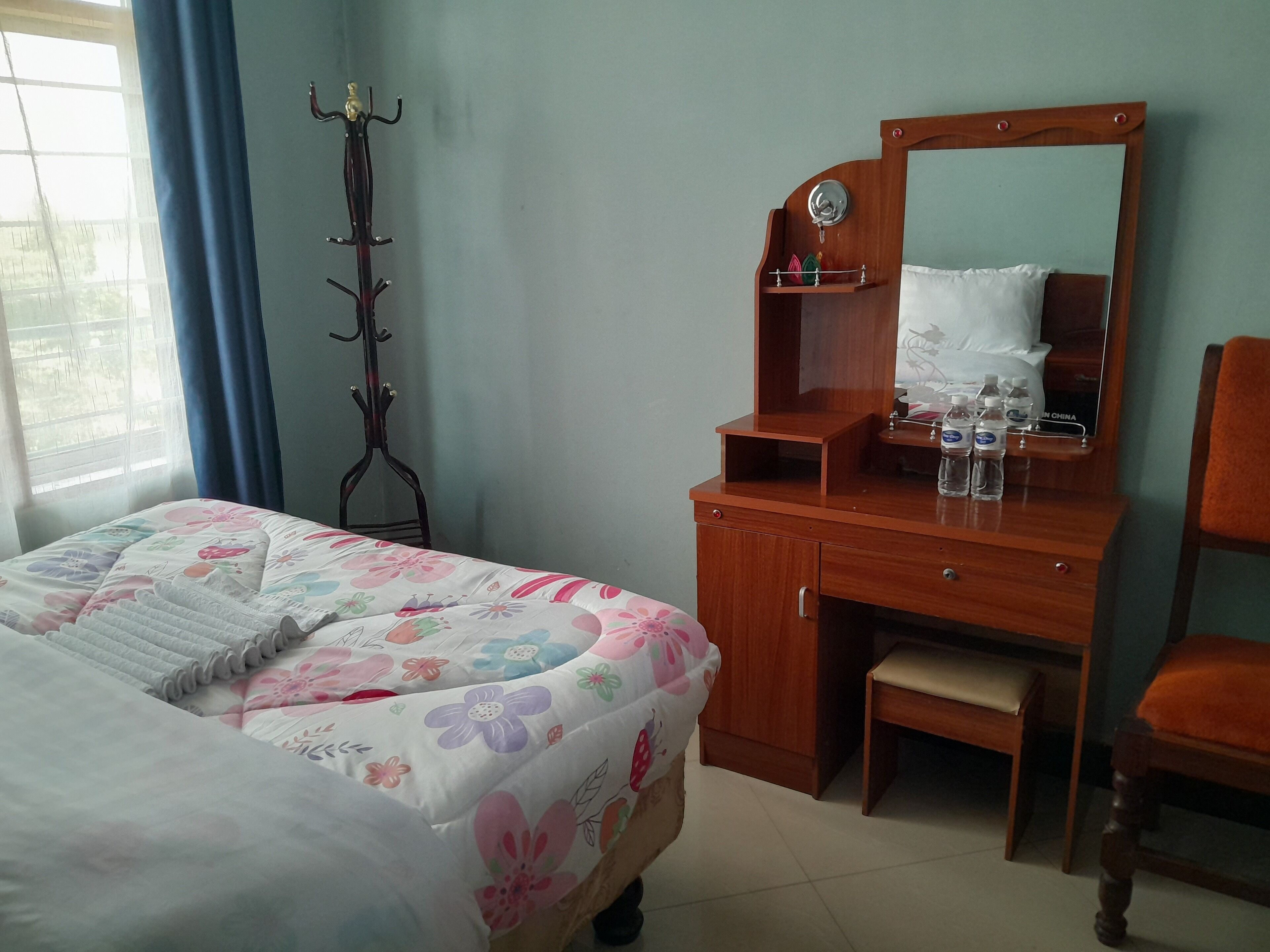 Un dormitorio con una cama, un aparador de madera, un espejo y un perchero.