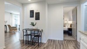 A modern kitchen with a dining area, featuring a wooden floor, white walls, and a small table with chairs.