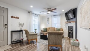 A modern living room with a sofa, chairs, a coffee table, a fireplace, and a flat-screen TV mounted on the wall.