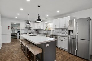 A modern kitchen with a central island, stainless steel appliances, pendant lighting, and a patterned backsplash. - Chic Escape:Pet Friendly w/Modern Charm & Waffles! (Orem)