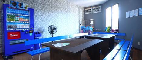 Una habitación con máquina expendedora, bancos azules y mesas.