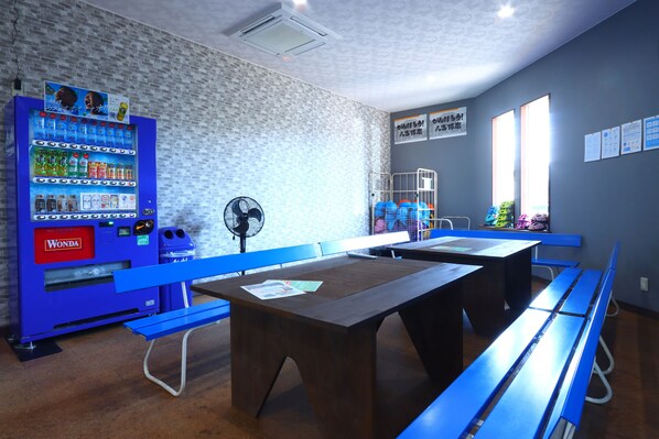 A room with a vending machine, blue benches, and tables. - Kumagawa Rafting Again (Hitoyoshi)