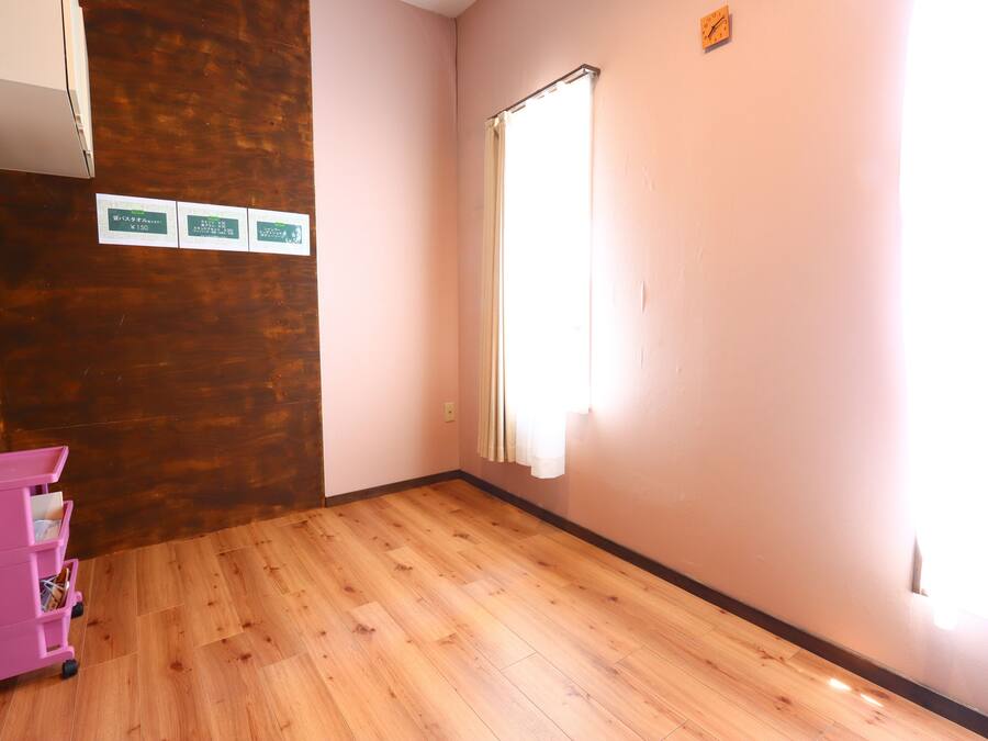Une pièce avec un plancher en bois, un chariot de rangement rose et une fenêtre avec des rideaux.