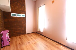Una habitación con piso de madera, un carrito de almacenamiento rosa y una ventana con cortinas.