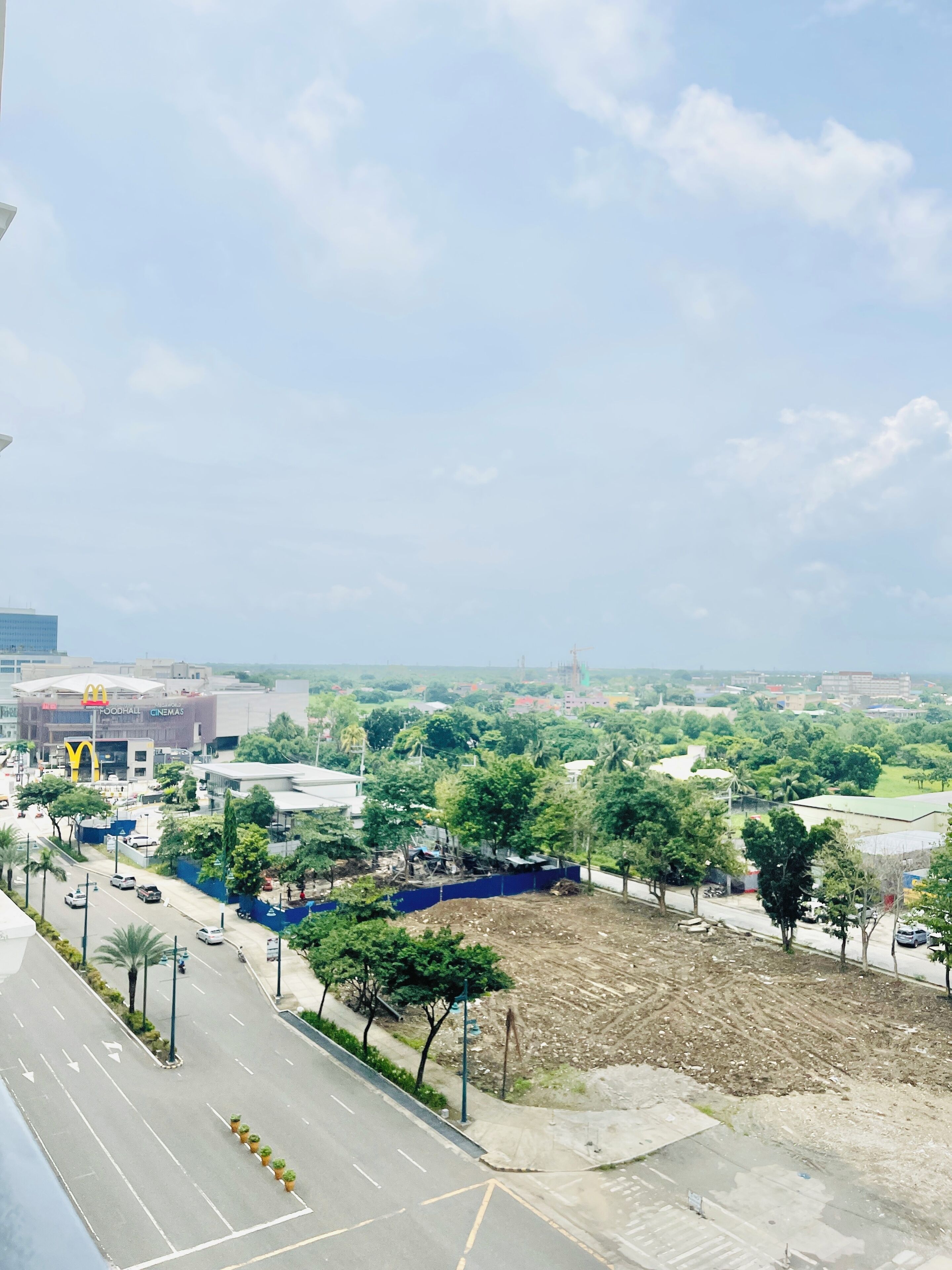 A view of a cityscape with a McDonald's and cinemas, a road with cars, and green areas with trees.