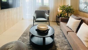 Un soggiorno moderno con una TV a schermo piatto, un divano, una poltrona, un tavolino da caffè e un'ampia finestra con tende.