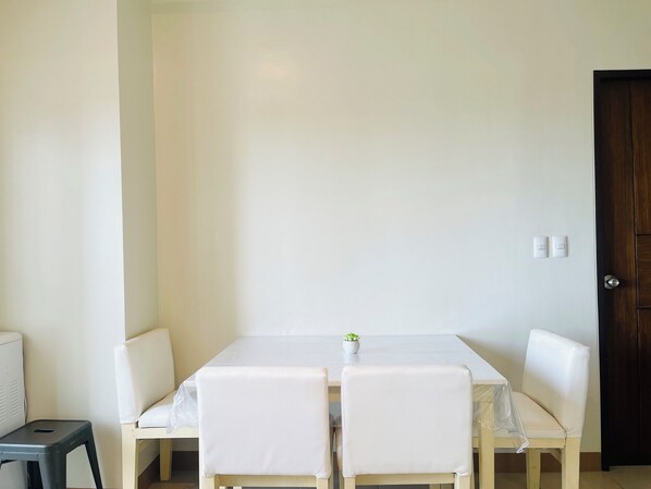 A room with a white table and two white chairs, a small potted plant on the table, and a dark wooden door.
