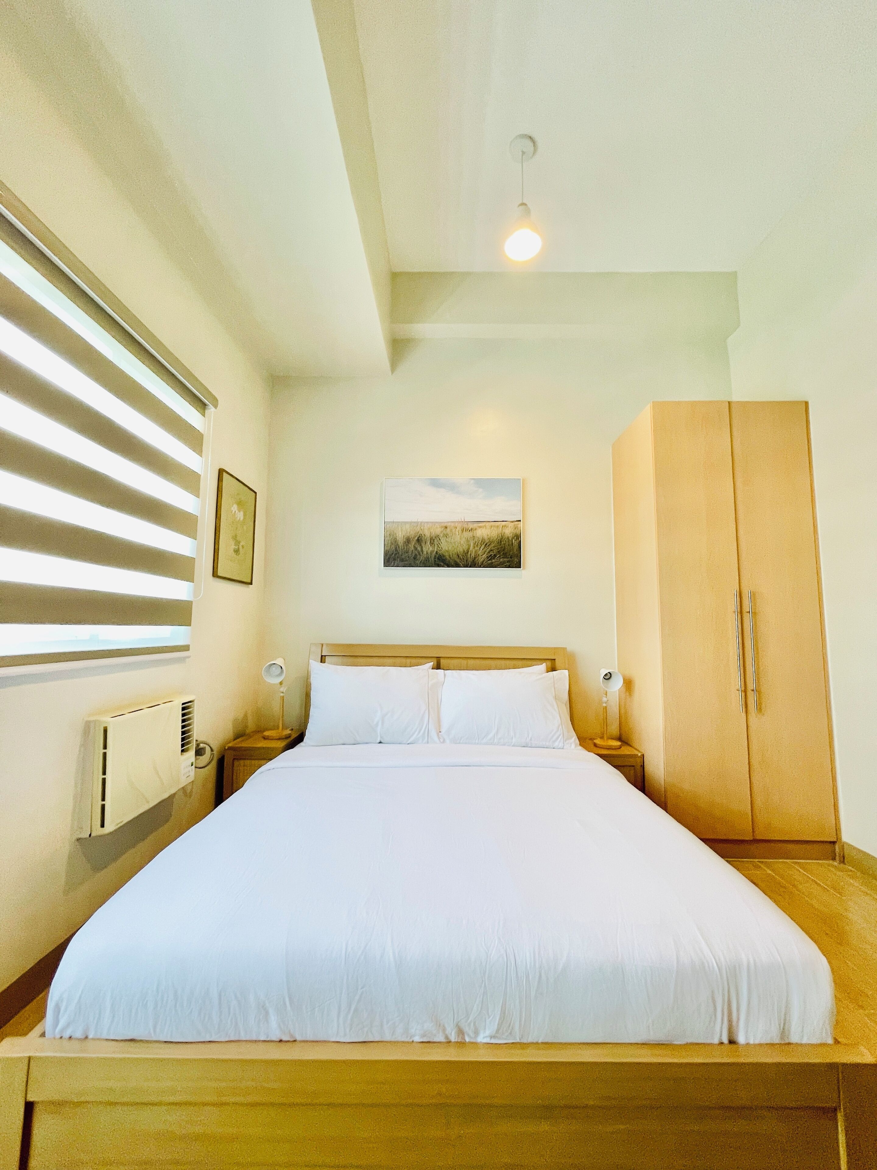 A bedroom with a large bed, a wooden wardrobe, a radiator, and a window with blinds.