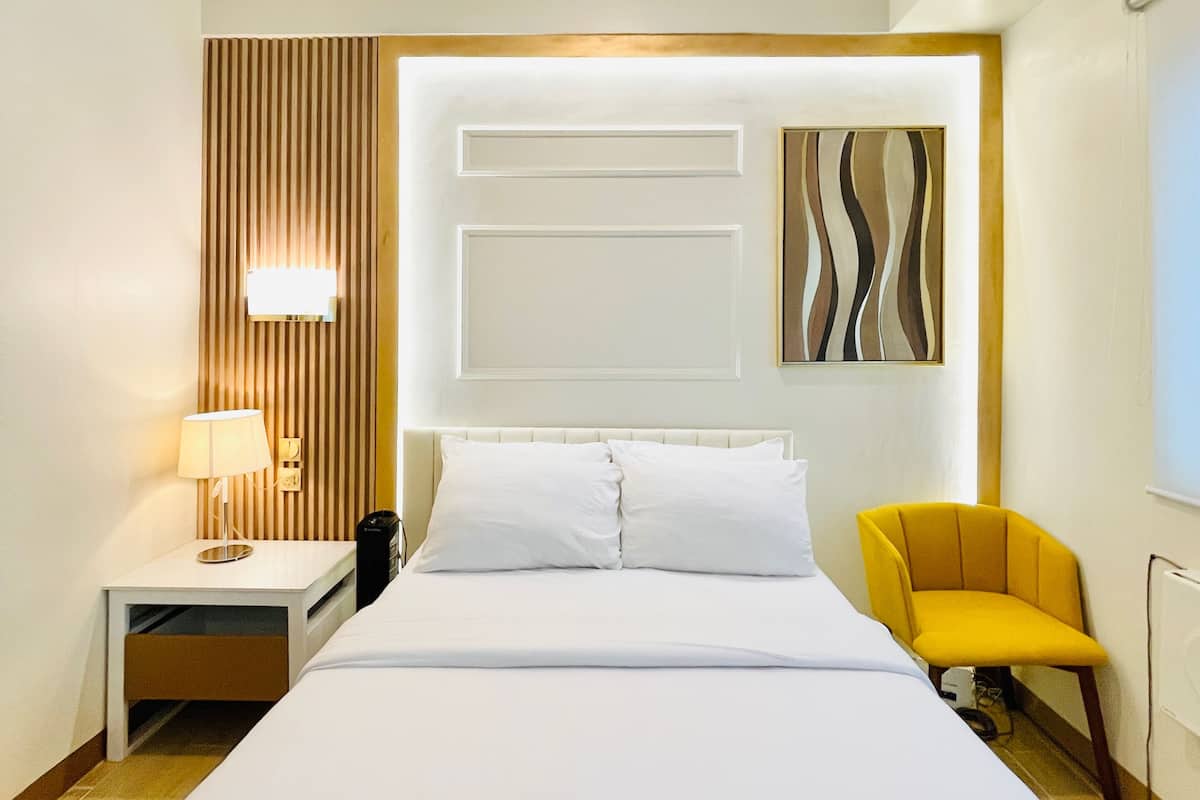 Une chambre d’hôtel avec un grand lit, une table de chevet avec une lampe, une chaise et une œuvre d’art accrochée au mur.