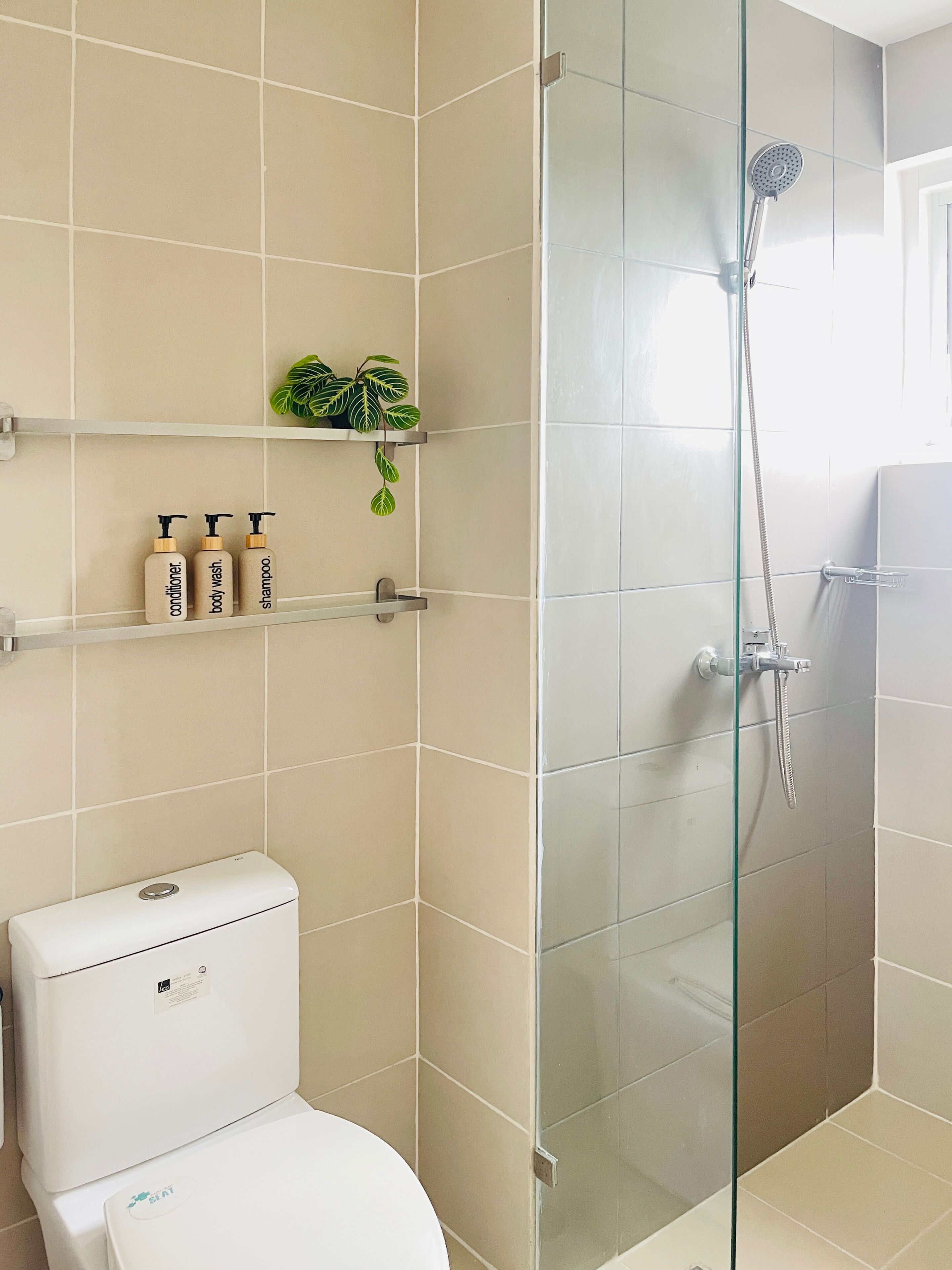 Moderni kylpyhuone, jossa on wc, lasiseinäinen suihku ja hyllyjä, joilla on hygieniatuotteita.