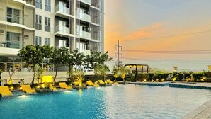 Una piscina con lettini, immersa nel verde e circondata da un edificio moderno con balconi.