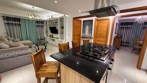 Eine moderne Küche mit Kochinsel, Holzsesseln, einem Esstisch und einer Wohnbereich mit Sofa und Vorhängen.