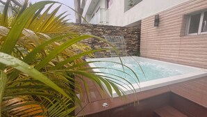Ein moderner Whirlpool im Freien mit Steinwand im Hintergrund und Wasserfall.