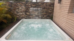 Ein Whirlpool mit Wasserfall, umgeben von einer Steinmauer und Palmen.