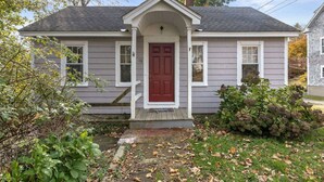 Une maison de plain-pied avec une porte d’entrée rouge, des boiseries blanches et un petit porche.