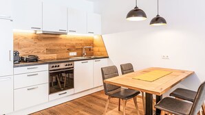 A modern kitchen with white cabinets, a wooden backsplash, and a dining area with a wooden table and chairs. - Lovely apartment for 4 guests with WIFI, TV, terrace and panoramic view (Brandstätter)