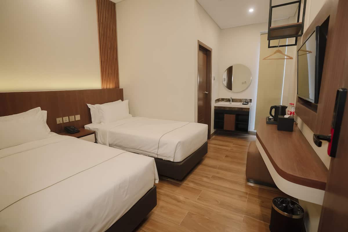 A hotel room with two beds, a wooden headboard, a small bathroom with a mirror, and a TV mounted on the wall.