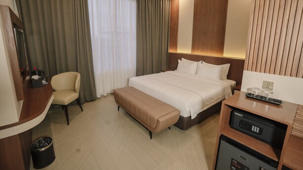 A hotel room with a bed, a desk, a chair, a bench, a trash bin, and a minibar. - Parkside's Hotel Palembang (Palembang)