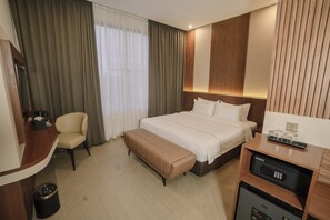 A hotel room with a bed, a desk, a chair, a bench, a trash bin, and a minibar. - Parkside's Hotel Palembang (Palembang)