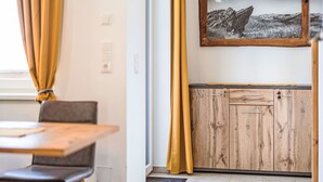 A modern interior with a wooden cabinet, a framed landscape photo, and a window with yellow curtains. - Nice apartment for 4 people with WIFI, TV, terrace and panoramic view (Brandstätter)