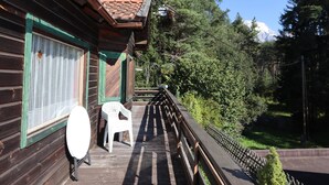 Una cabaña de madera con un balcón, una silla de plástico blanca y una mesa redonda.