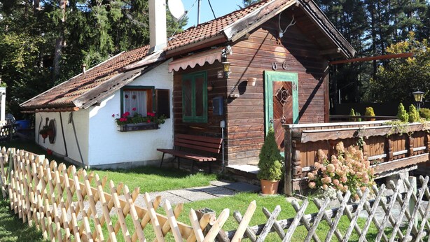 Una casa de madera rústica con techo inclinado, un pequeño porche y fachada blanca.