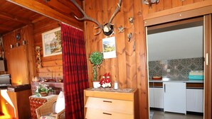 Un acogedor interior de cabaña de madera con comedor, cocina y una cortina roja de cuadros.
