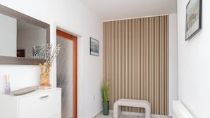 A hallway with a white dresser, a bench, a potted plant, a mirror, and a striped wall. - Spacious 2 Bedroom Apartment With Balcony (Sibenik)