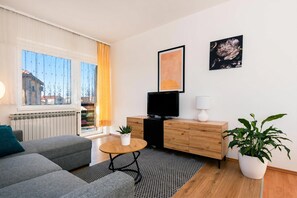 Una sala de estar moderna con un sofá, una mesita redonda pequeña, un televisor, un aparador, una planta en maceta y obras de arte en la pared.
