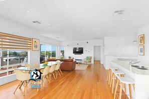 A spacious living area with a dining table, sofas, and a kitchen area with a bar.