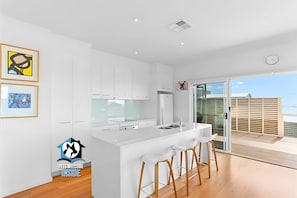 A modern kitchen with white cabinetry, a central island with bar stools, and a sliding glass door leading to a balcony.