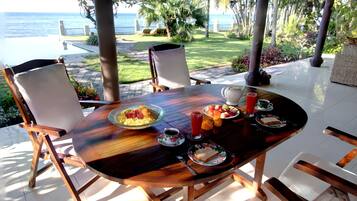 An outdoor dining area with a table set for two, overlooking a pool and the ocean.