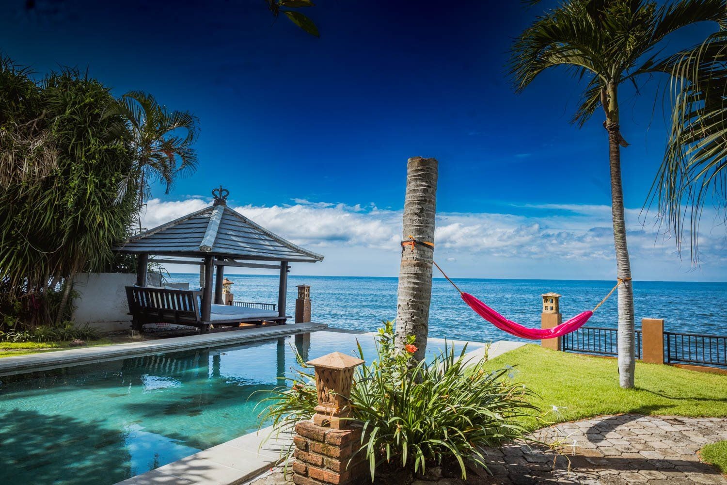 A poolside area with a gazebo, a hammock, and a view of the ocean.
