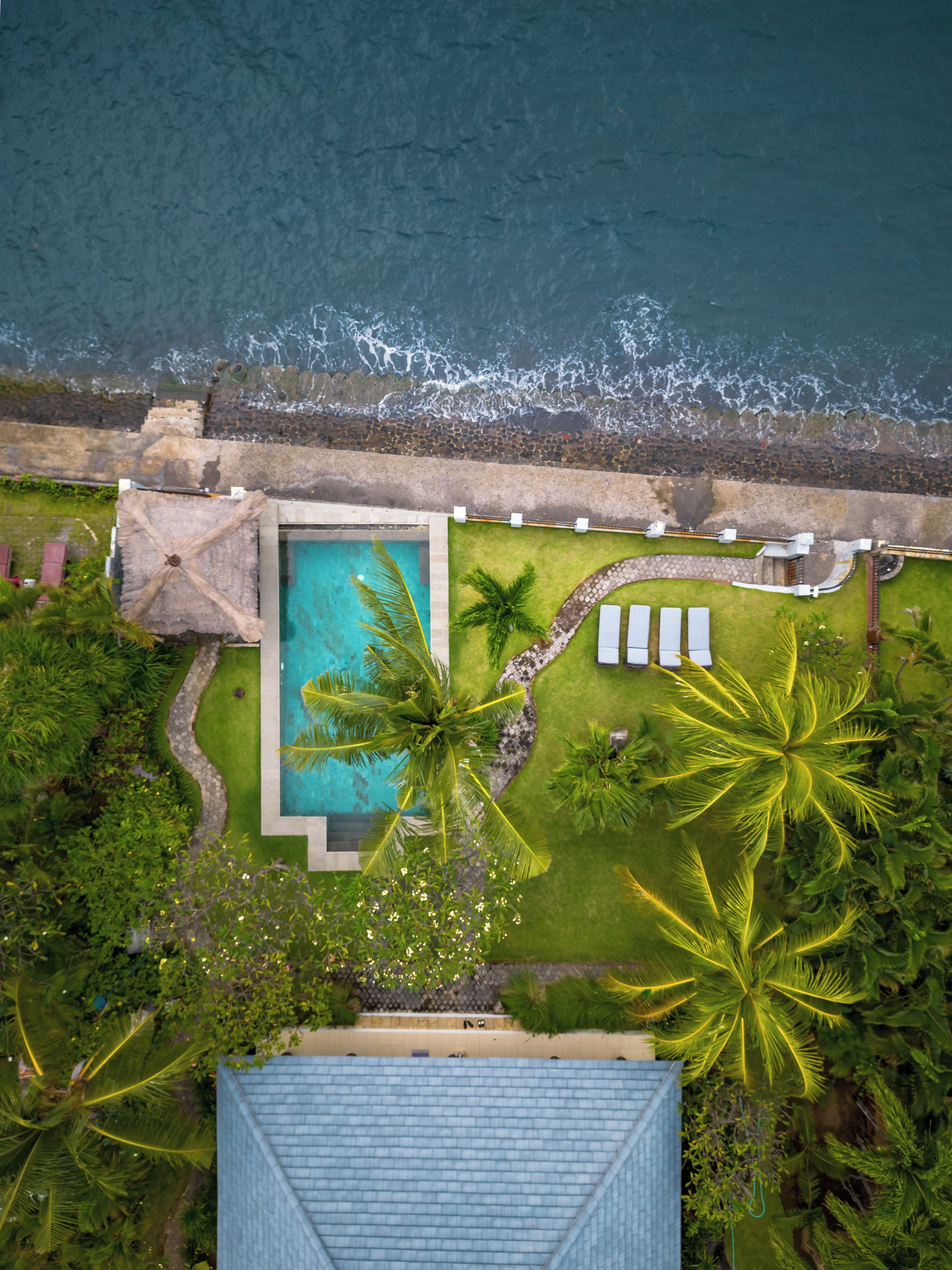 Luftaufnahme eines Resorts mit Schwimmbad, Palmen und Strand.