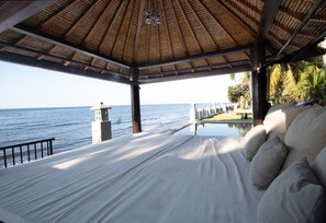 Een kamer aan het strand met een bed, uitzicht op de zee, een zwembad en een rieten dak.