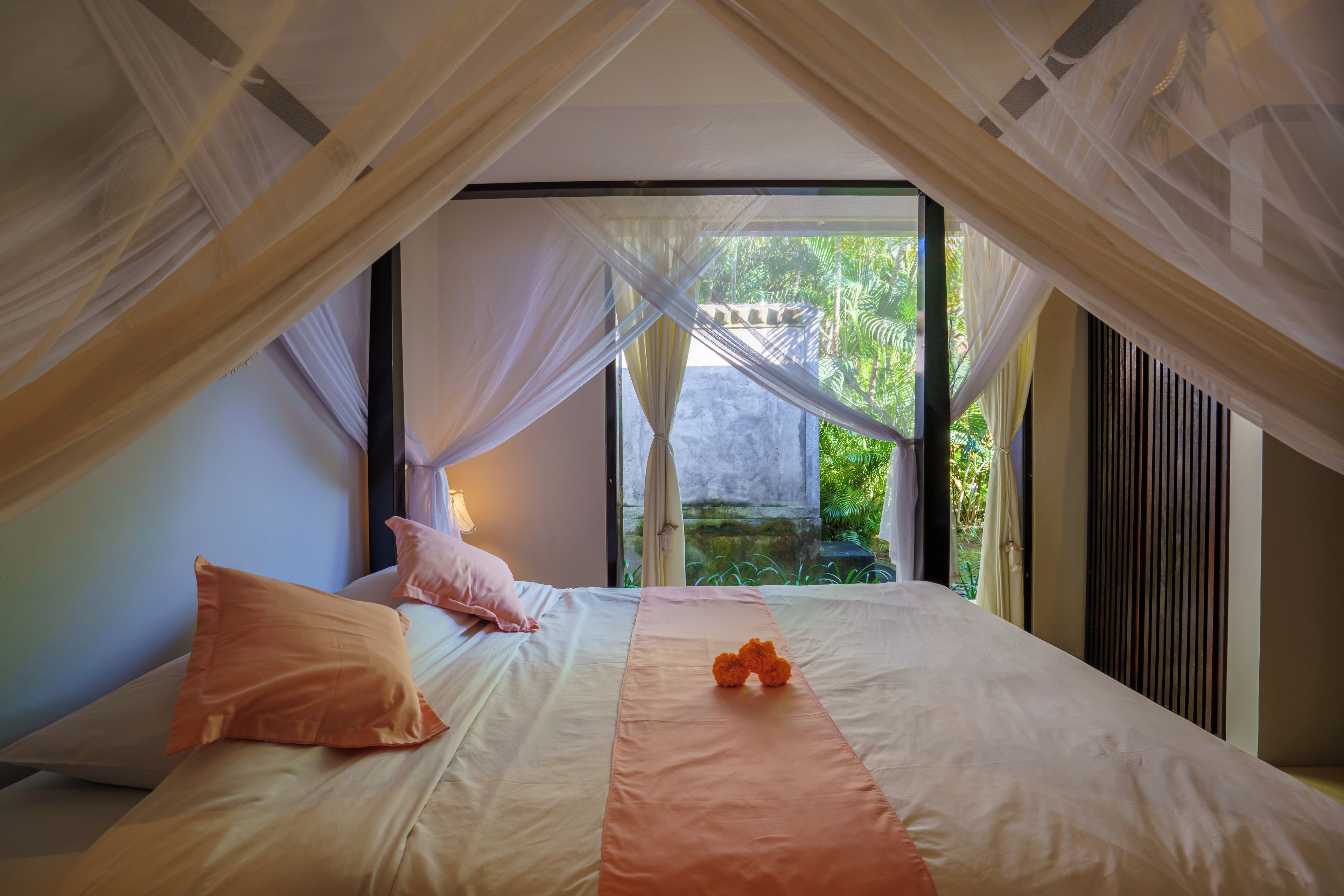 Un dormitorio con cama, almohadas, un objeto decorativo naranja y vistas al exterior.