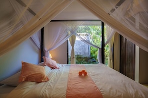 Ein Schlafzimmer mit Bett, Kissen, einem orangefarbenen Dekorationsgegenstand und Blick auf Grünflächen.
