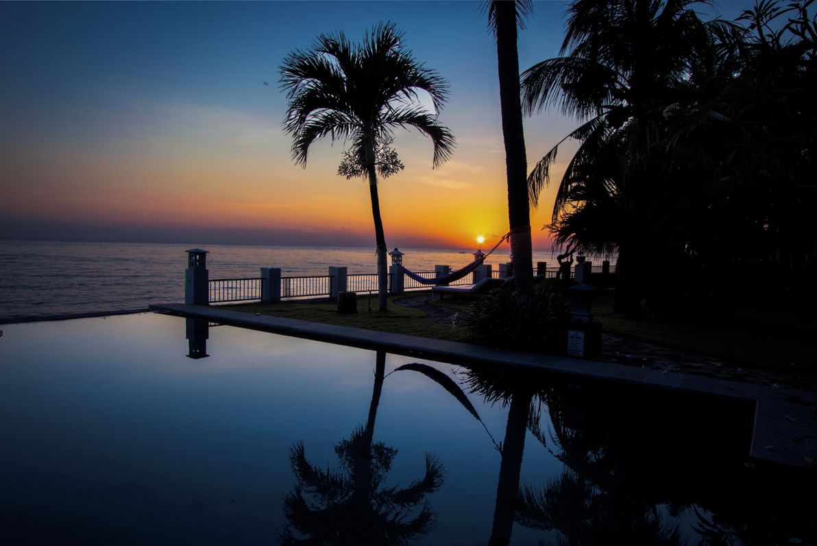 Vista al tramonto da una zona piscina, con palme e un'amaca.