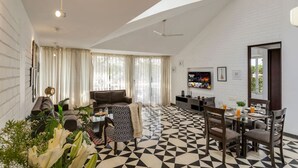 Ein modernes Wohnzimmer mit hohen Decken, einem Essbereich mit geometrischem Muster im Boden und einem an der Wand befestigten Fernseher.