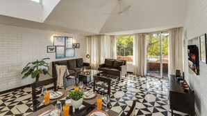 Ein großzügiger Wohnbereich mit hoher Decke, Deckenventilator, gro ßem Fenster mit Vorhängen, Boden in Schwarz-Weiß-Muster und einer Sitzecke mit Sofas und Couchtisch.