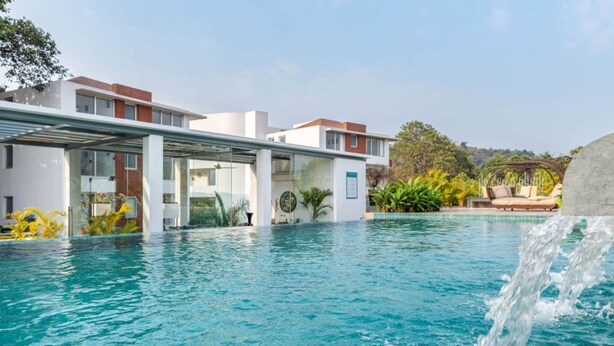 Ein Schwimmbecken mit Wasserfall, umgeben von moderner Architektur und üppiger Vegetation.